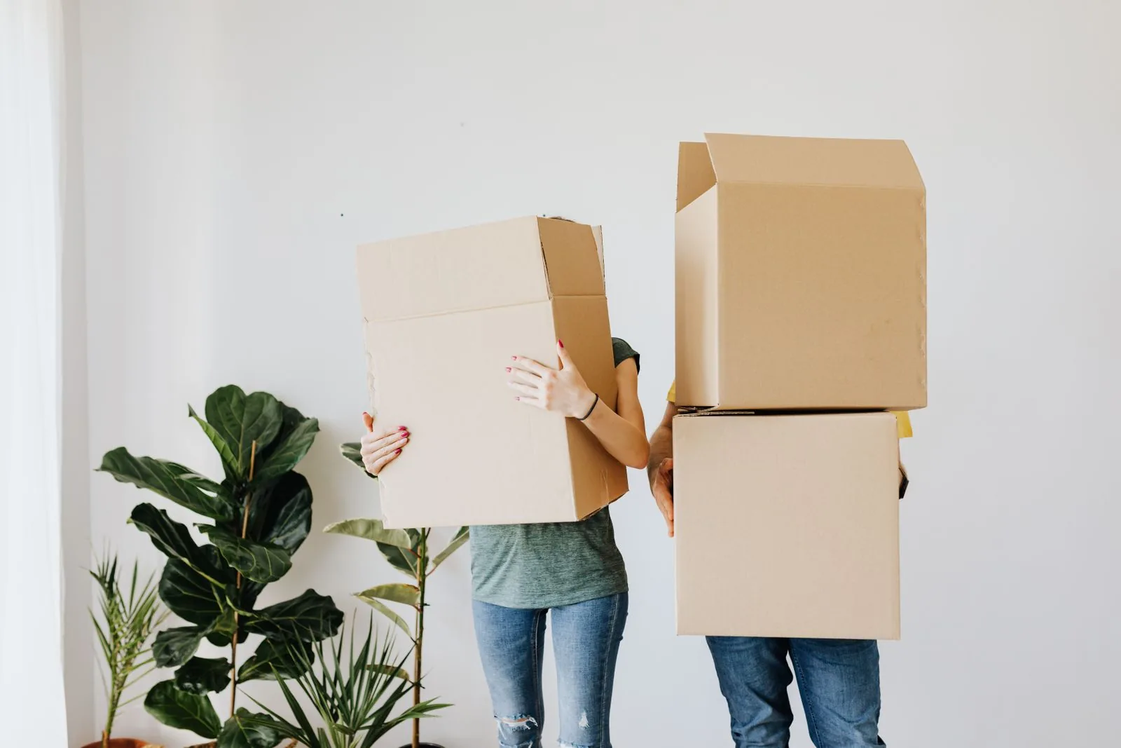 Couple carrying stacked cardboard boxes through their living room