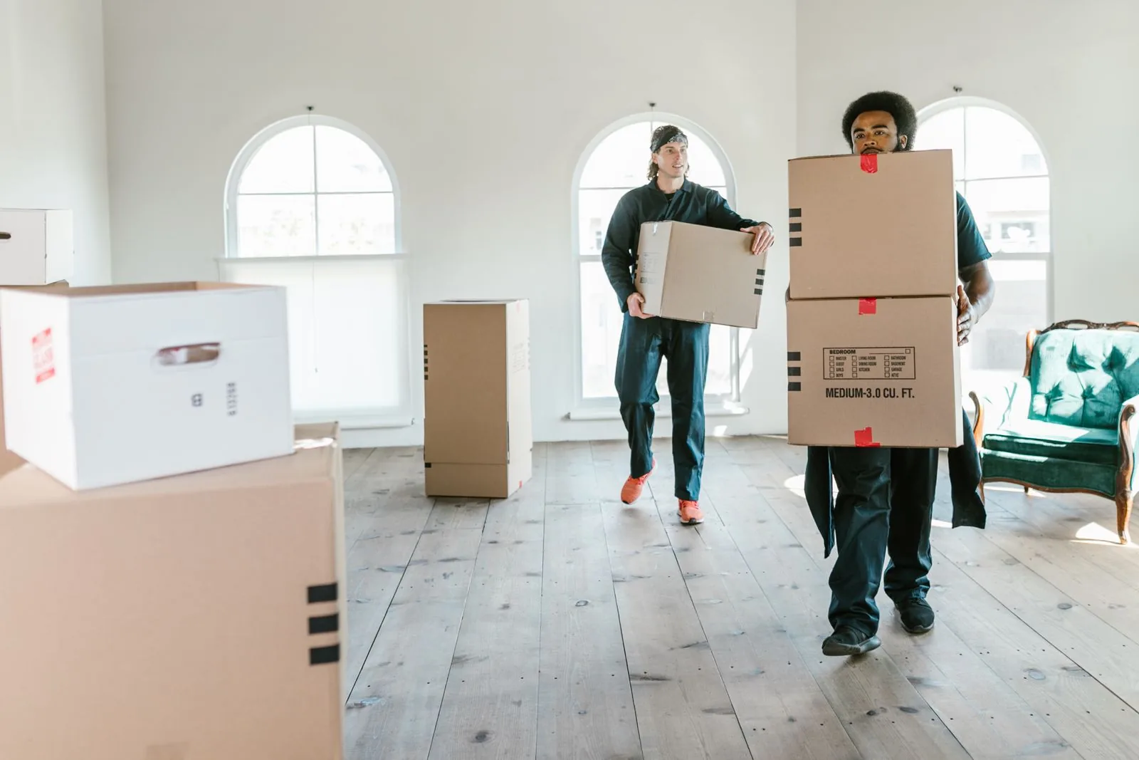 Two movers carrying cardboard boxes into an empty, sunlit home