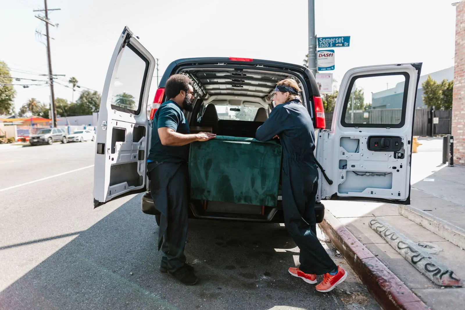 Two movers loading a sofa into the back of a moving van on a city street