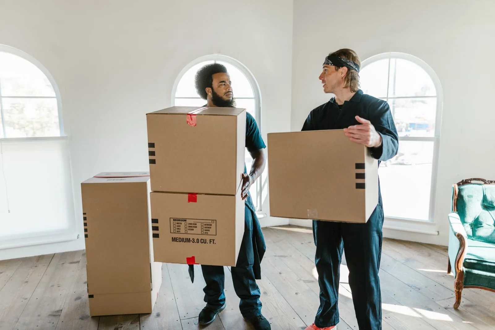 Two movers in work uniforms carrying labeled moving boxes